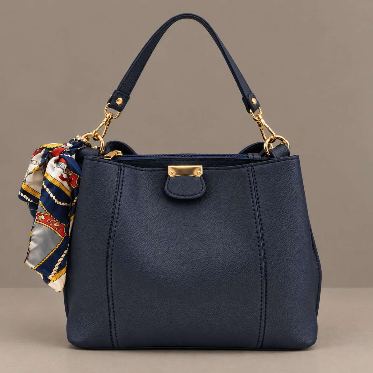 Navy top handle bag with a gold front tab and a printed scarf tied to the handle