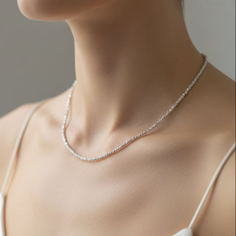Silver bead necklace worn by a person on a grey background
