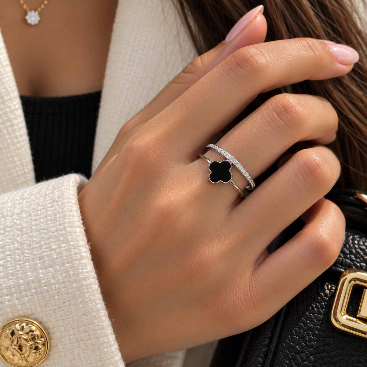 Hand wearing a silver double band ring with a black clover and a row of crystals, holding a black bag