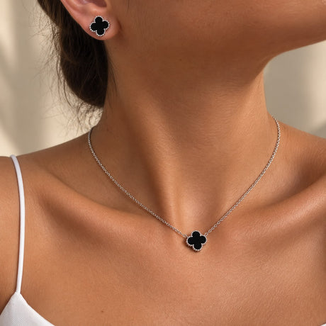 Silver tone necklace and stud earrings with black clover charms worn together, close up