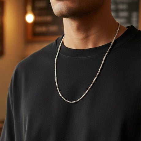 Silver box chain necklace worn over a black tee in a warm lit cafe