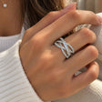 Hand wearing a wide silver criss cross ring with pave bands over a row of baguette crystals
