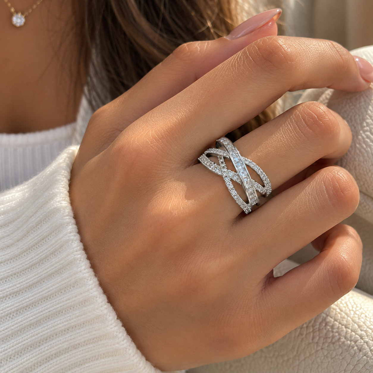 Hand wearing a wide silver criss cross ring with pave bands over a row of baguette crystals