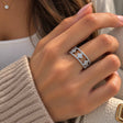 Hand wearing a wide silver openwork ring with crystal clovers, beside a beige knit sleeve
