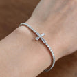 Silver tennis bracelet with a baguette crystal cross worn on the wrist in soft daylight
