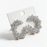 Pair of silver tone crystal wreath statement earrings resting on a white card
