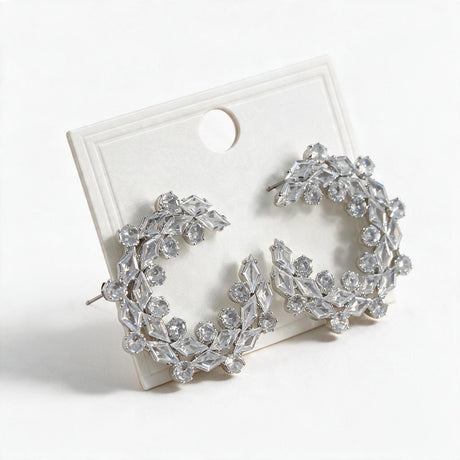 Pair of silver tone crystal wreath statement earrings resting on a white card