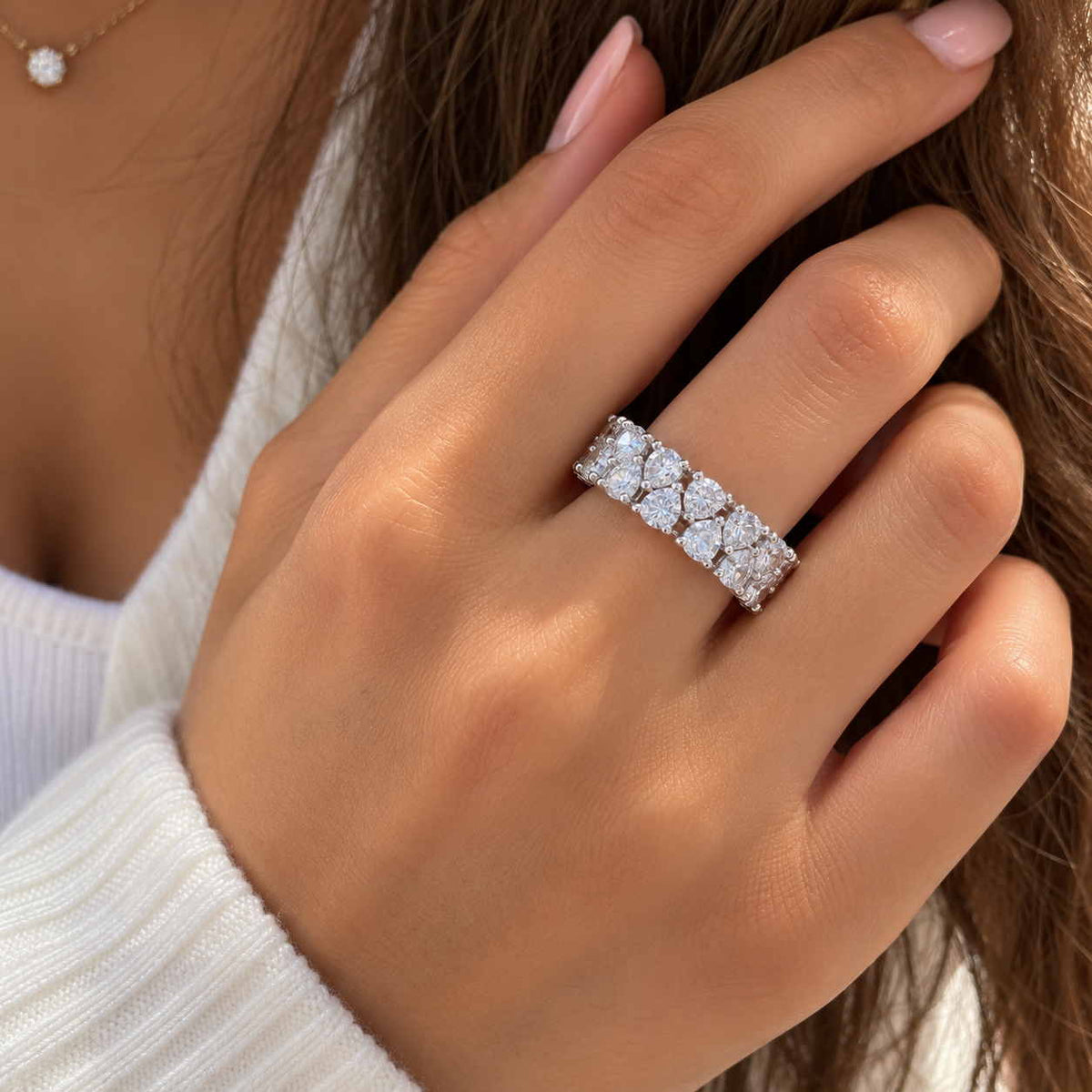 Hand wearing a wide silver ring with two rows of large round crystals, fingers in long brown hair
