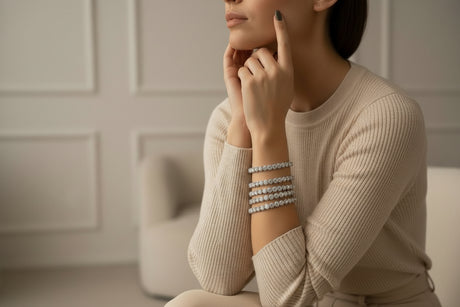 Woman wearing a beige sweater and multiple silver bracelets in a neutral setting