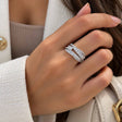 Hand wearing a silver crossover ring with layered rows of round and square crystals, holding a cream bag