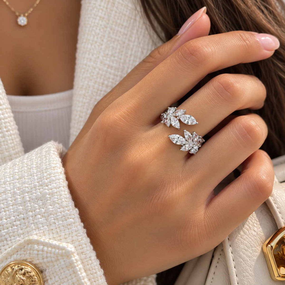 Hand wearing a silver open ring with two leaf shaped clusters of marquise crystals on a cream jacket