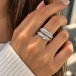 Hand wearing a wide silver ring with sweeping rows of round and baguette crystals, over a white knit sleeve