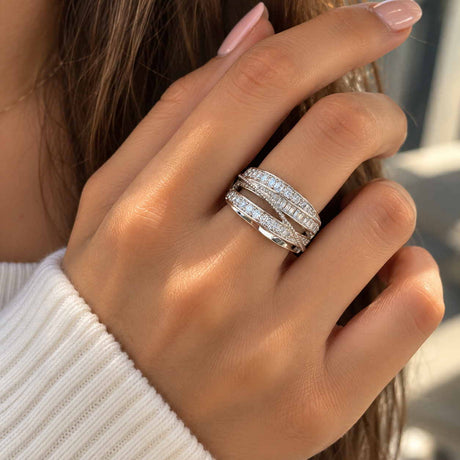 Hand wearing a wide silver ring with sweeping rows of round and baguette crystals, over a white knit sleeve