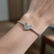 Silver tennis bracelet with a heart charm, half crystal and half polished, on the wrist