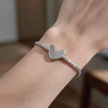 Silver tennis bracelet with a heart charm, half crystal and half polished, on the wrist