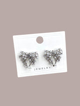 Pair of silver bow-shaped earrings on a white card with 'Jewelry' text against a beige background