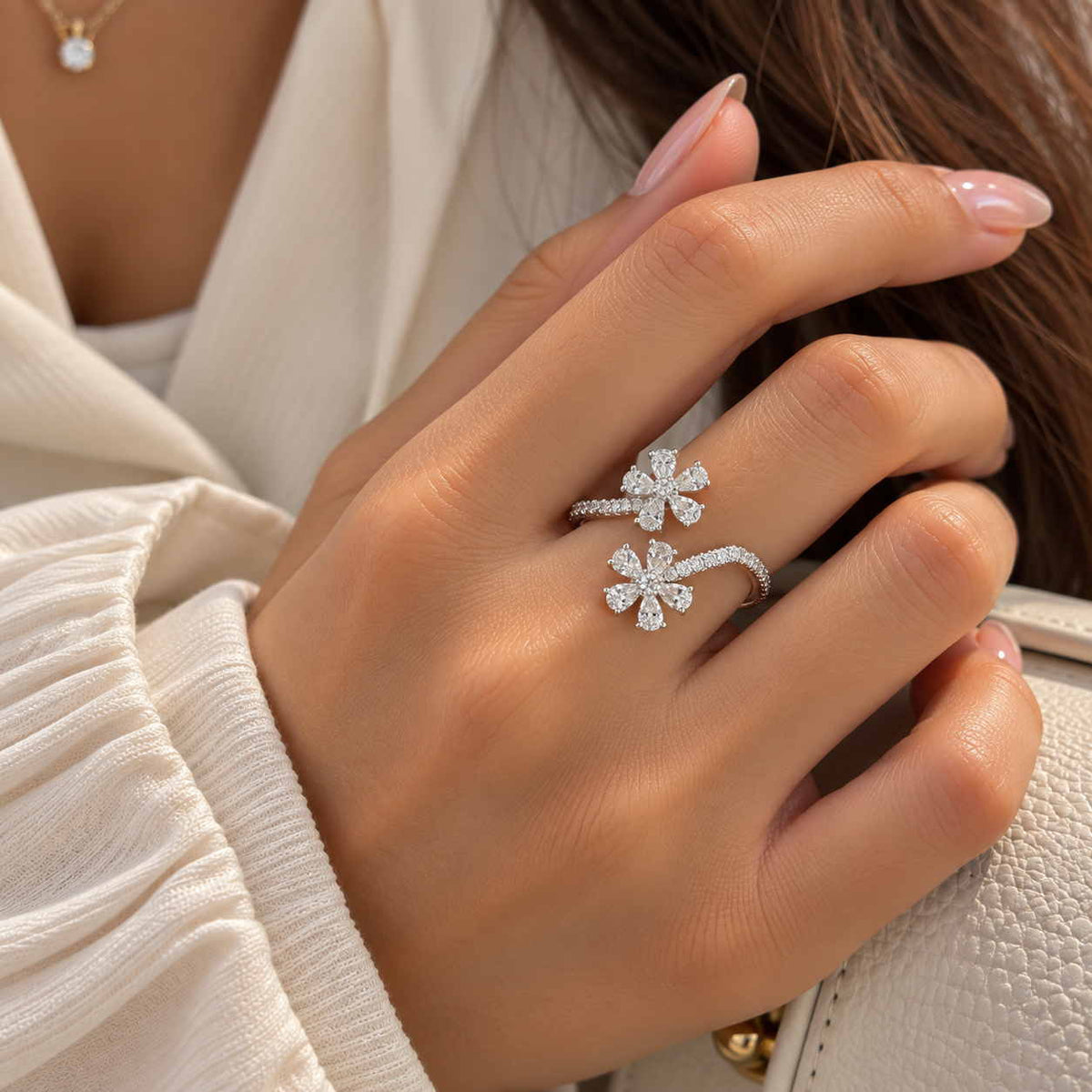 Hand wearing a silver open ring with two crystal flowers on a pave band, against a cream blouse