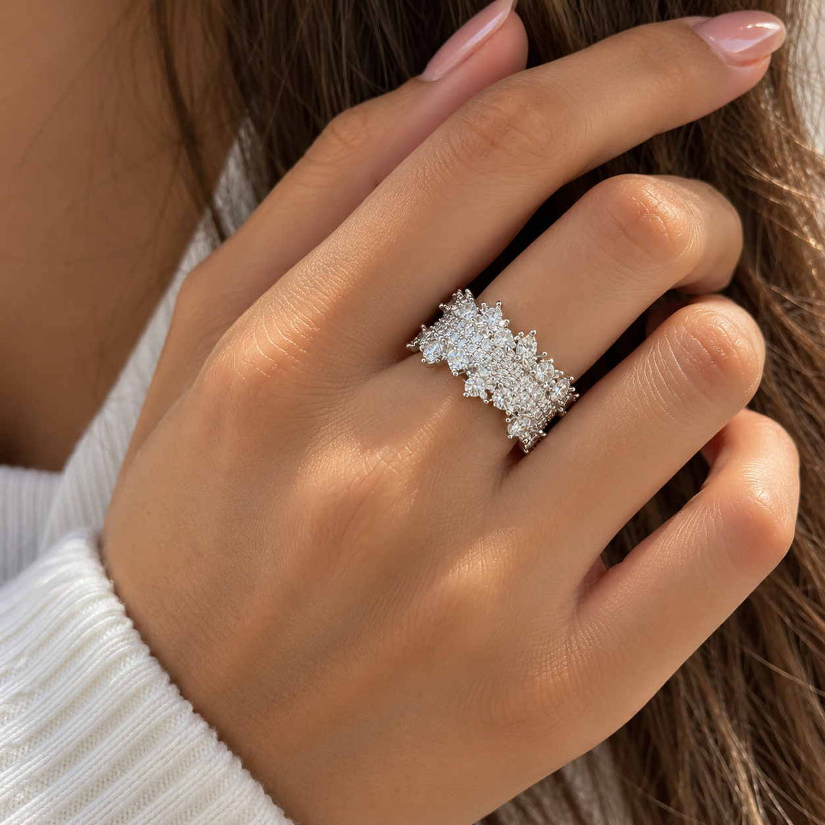 Hand wearing a wide silver band ring covered in clustered round and pear crystals, fingers in long hair