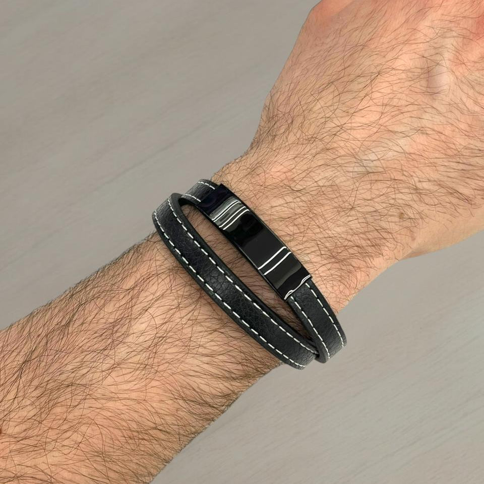 Black leather bracelet with metal clasp on a wrist against a grey background