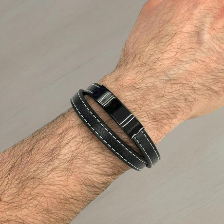 Black leather bracelet with metal clasp on a wrist against a grey background