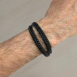 Black braided bracelet on a wrist against a neutral background