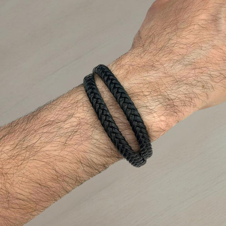 Black braided bracelet on a wrist against a neutral background