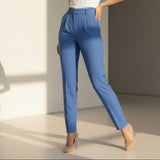 Woman wearing a white top and sky blue pants standing against a neutral wall