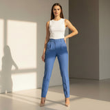 Woman wearing sky blue pants and a white top standing against a neutral wall