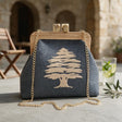 Slate blue clutch with an embroidered cedar and wooden frame beside a glass of lemonade in a stone courtyard
