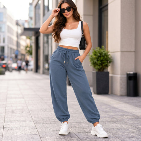 Woman in slate blue cuffed joggers with a drawstring waist, a white tank crop top and white sneakers