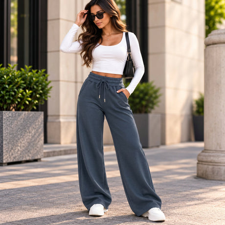 Woman in slate blue wide leg sweatpants with a drawstring waist, a white crop top and white sneakers