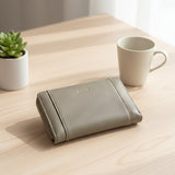 Beige wallet on a wooden table with a white mug and plant in the background