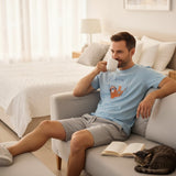 Sloth print pyjama set worn on a sofa with a cat and a mug of coffee