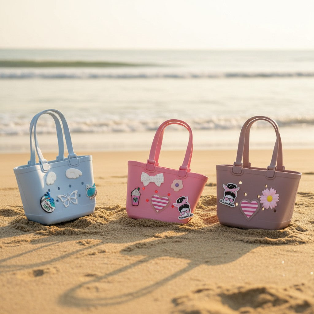 Baby blue, bubblegum pink and mauve EVA beach totes lined up on sand with charm decorations