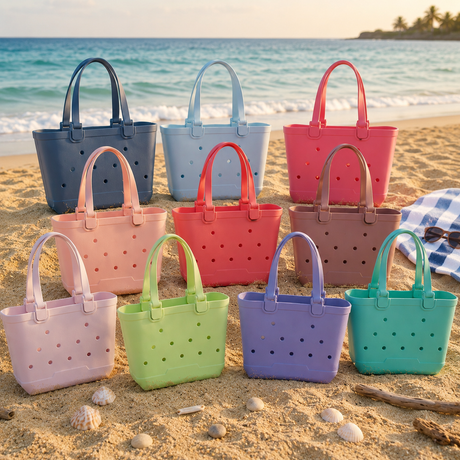 Ten waterproof EVA kids tote bags in a full colour range arranged on sand with a striped towel