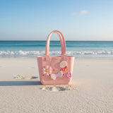 Peachy pink kids tote standing on bright white sand with clear blue sky and turquoise water behind