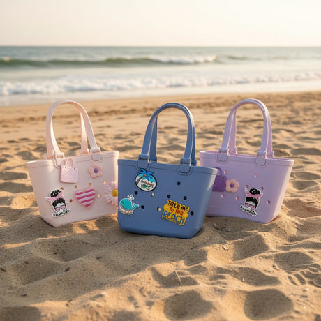 Three kids waterproof EVA tote bags in blush pink, denim blue and lilac with rubber charms on sand