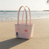 Pale pink rubber beach tote with matching handles and daisy, bow, lollipop and handbag charms
