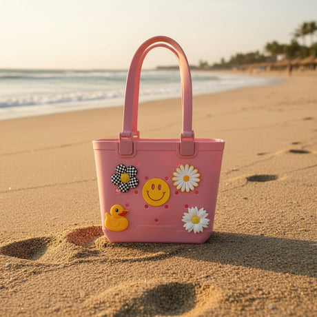 Rose pink tote with rubber duck, smiley face, checkerboard flower and two white daisy charms on a beach