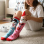 Girl wearing mismatched pink and blue snowman knee high Christmas socks on a rug