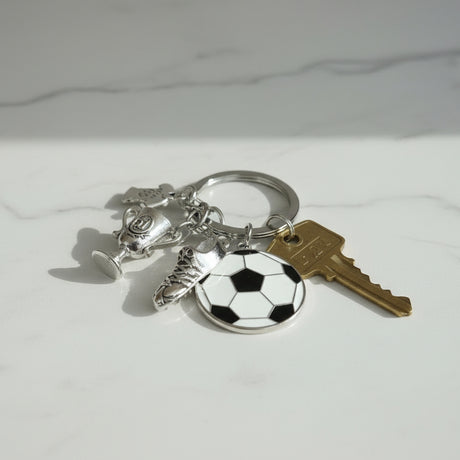 Soccer keychain with trophy, boot, and football charms on white marble