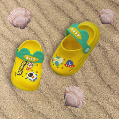 Kids yellow clogs with space charms and a green back strap on sand, Jack Gifts Online Lebanon
