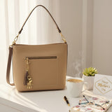 Beige shoulder bag with a gold tassel charm beside a coffee cup and a Mother's Day card