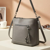 Grey shoulder bag seen from the side with its long adjustable strap and silver tassel
