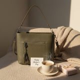 Olive shoulder bag resting on a knit throw with a coffee cup and a Mother's Day card