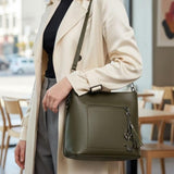 Olive bag worn crossbody with a cream trench coat and grey trousers