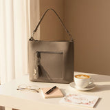 Pewter grey shoulder bag on a desk with reading glasses, a notebook and a latte