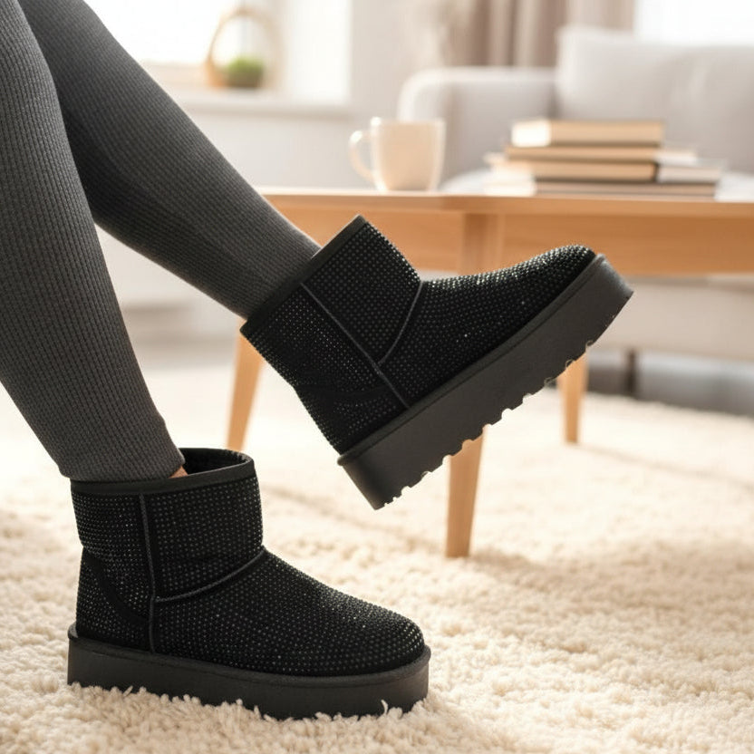 Sparkly black winter boots worn indoors with a blurred background of a living room.