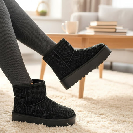 Sparkly black winter boots worn indoors with a blurred background of a living room.