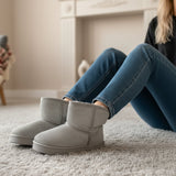 Person wearing gray textured boots and blue jeans sitting on a carpeted floor.